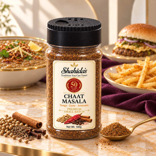 Shahida's Kitchen Chaat Masala 100g jar on marble with fries, a burger, haleem and whole spices